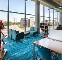 Desks, chairs, and book display next to wall of windows
